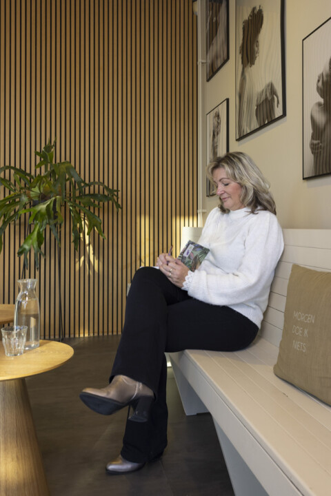 Manon zittend op een houten witte bank, met notitieboekje waar ze aantekeningen in maakt voor haar coach sessies vanuit Oud Beijerland en Barendrecht
